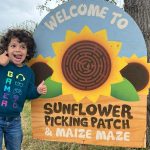 an excited child stands by the sign at the entrance of the maize with thumbs up